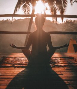Anxiety reduction as a woman sits on a sunlit deck in a traditional meditation pose.